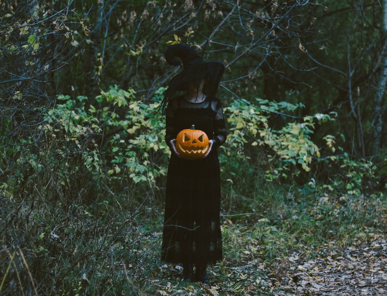 A witch holding a carved pumpkin in the woods