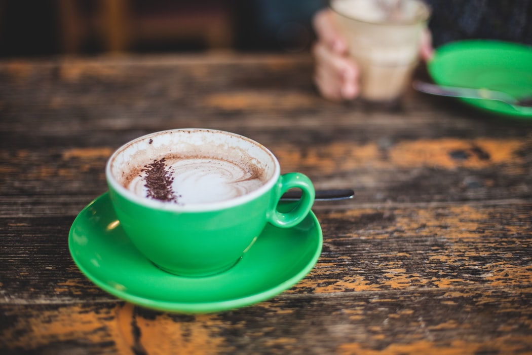 A cappuccino in a green cup and saucer on a wooden table.