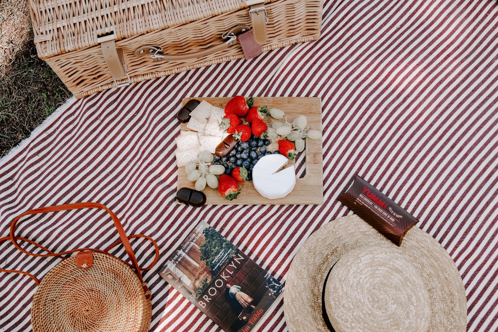 A book, a hat and a picnic basket on a picnic blanket.