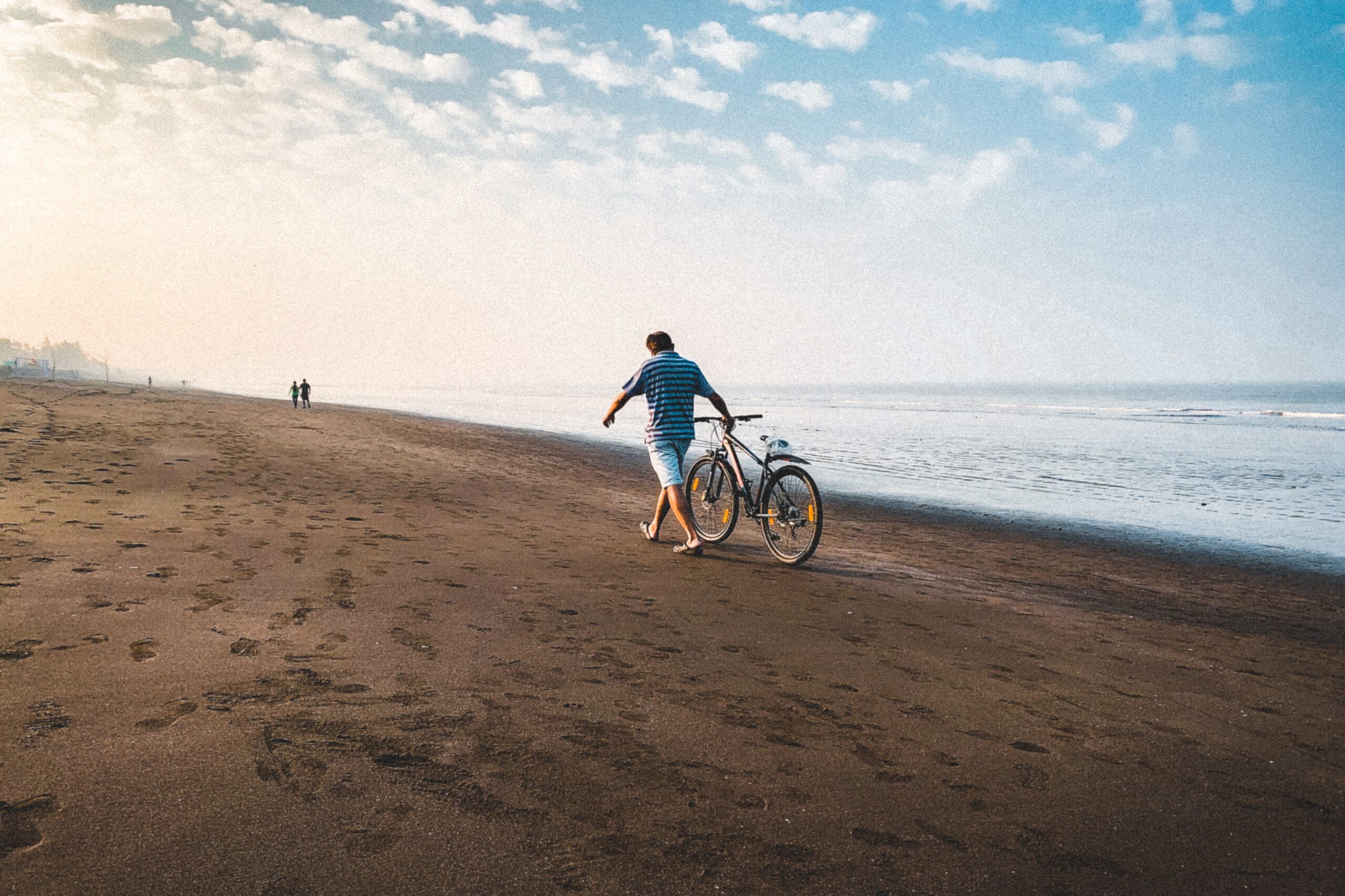 man walking bike on the beach