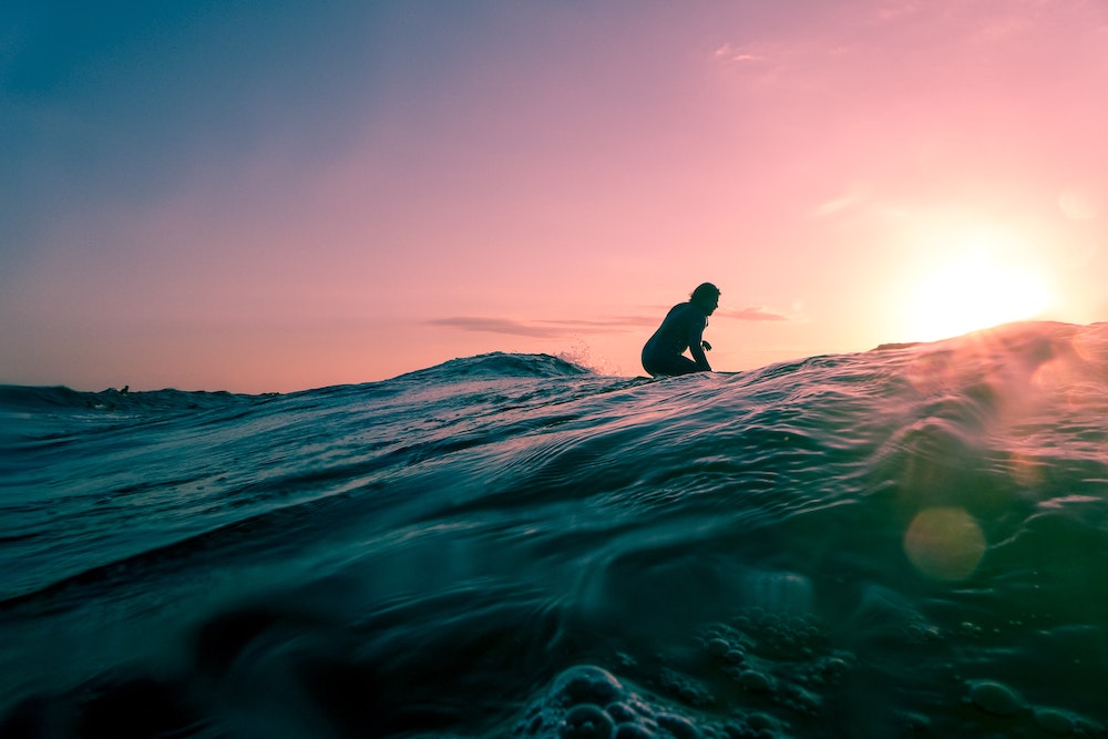 A surfer catching a wave in a purple sunset